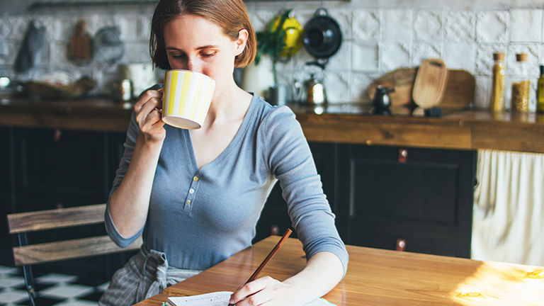 Woman drinks coffee while doing her budgeting to account for clothing inflation.