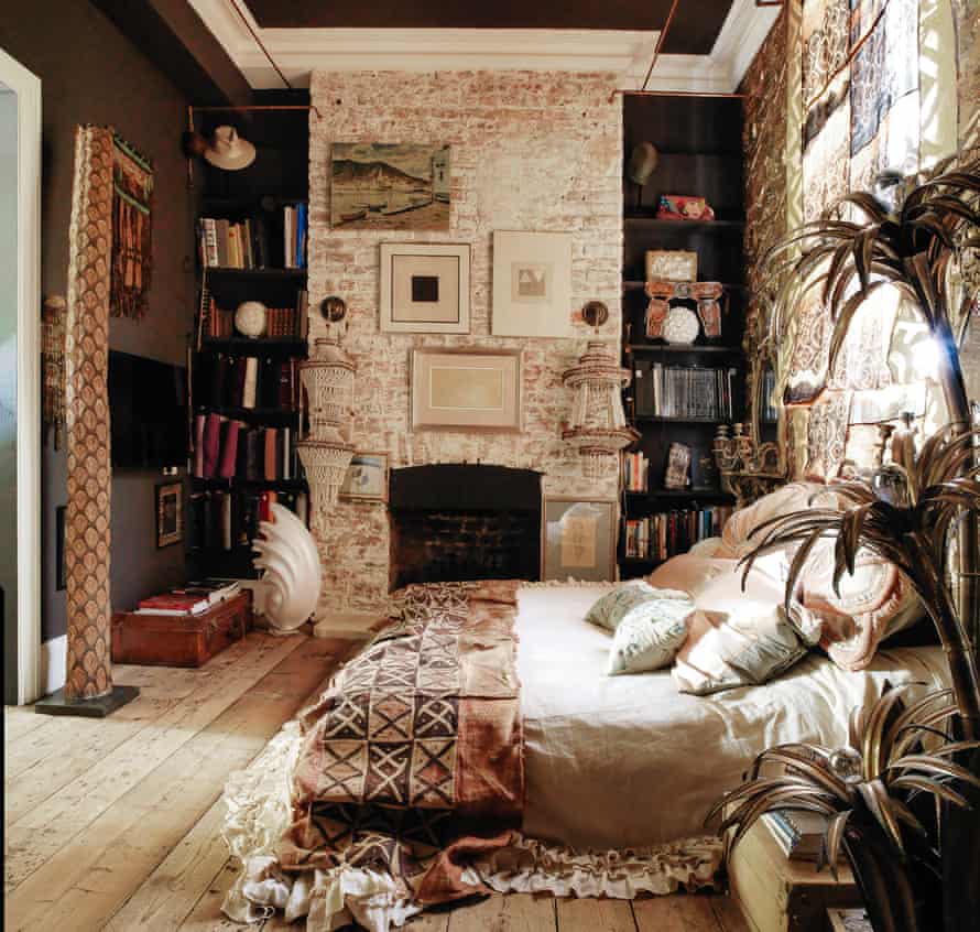 A bedroom with a fading whitewashed brick wall, a black wall and ceiling, and a double bed with cushions and a throw blanket