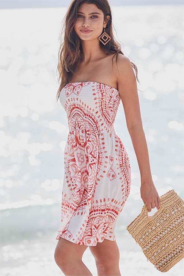 Model wears white and orange beach coverup in front of the ocean.