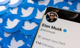 An image of a smartphone featuring Elon Musk’s Twitter page, with the Twitter “birds” in the background