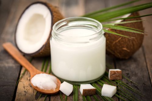 coconut oil in a jar and on a spoon with pieces of coconut around it