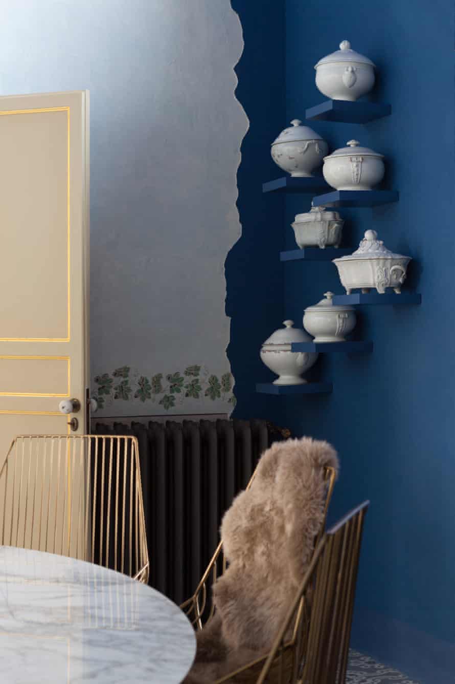 A wall painted blue with pots on small shelves going up the wall