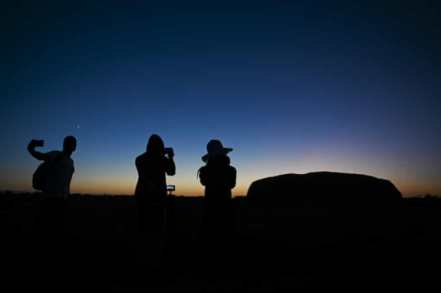 Tourists take pictures of Uluru just before sunrise.