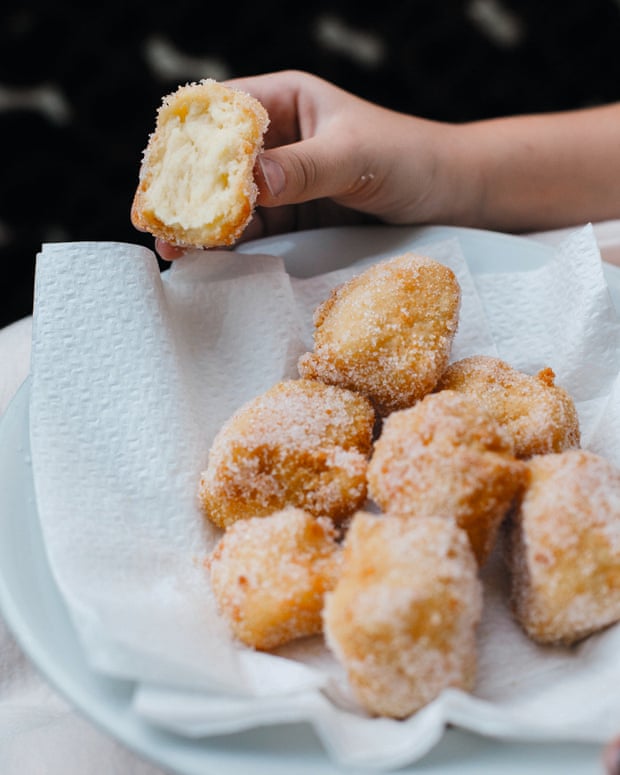 A plate of crema fritta. The fried custard portions are covered in sugar and sitting on a piece of paper towel on the plate. A hand is holding a half-eaten one