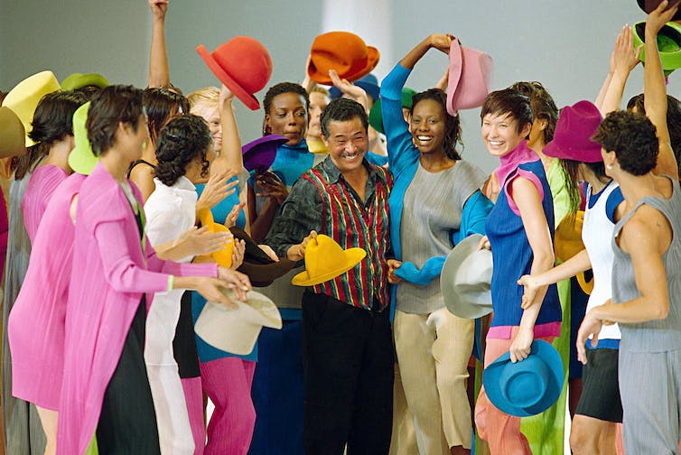 Models in colorful clothes surround Japanese designer Issey Miyake