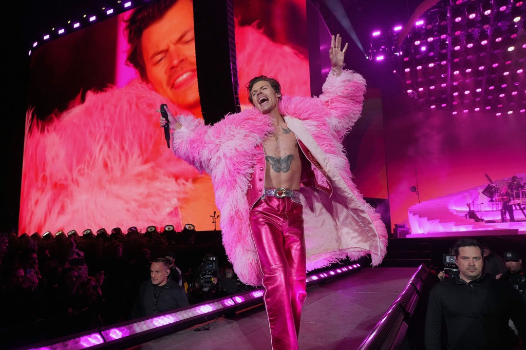 Harry Styles wearing a feathery hot pink jacket and matching pink pants. Fans feel inclined to match, showing up in feather boas.