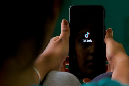 A woman holds a smartphone with the TikTok logo showing on a black background.