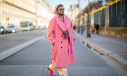 A person wearing cream pants, pink shoes and a long pink wool coat, walking along a street in Paris in the afternoon light