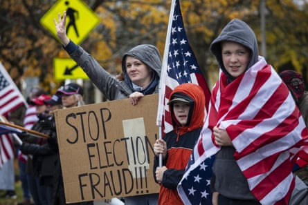 Two young children holding big American flags stand next to a woman holding a sign that reads 'Stop election fraud!!!'