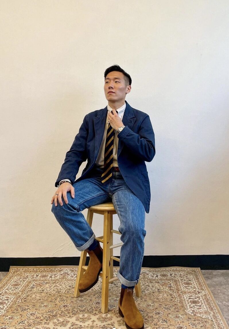 Man sitting on a stool dressed in a blazer, tie and jeans