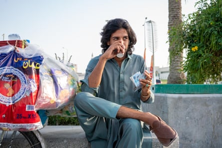 A man sits drinking tea from a paper cup by the waterfront in Doha, Qatar. He has a different coloured ring on each finger.