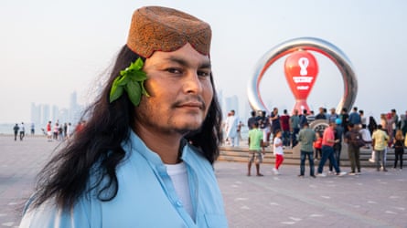 A man with long dark hair wearing a blue shirt and a brown cap on the Corniche in Doha, Qatar.