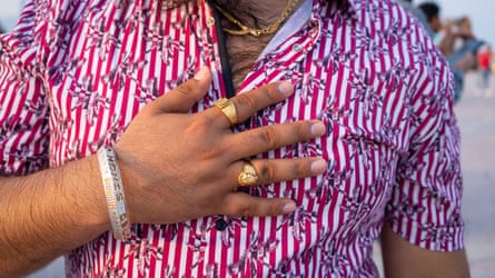 Close-up image of migrant worker in Qatar during his leisure time wearing a red-and-white striped shirt, with gold jewellery on his fingers.