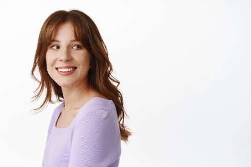 A young woman with ling red hair wearing a purple sweater against a white background.