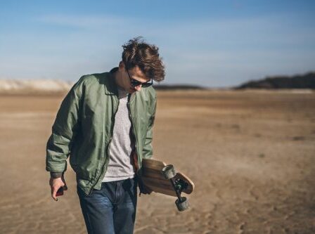 Young rebelious skater with his board, walking alone in a bomber jacket