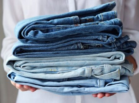 Person holding a stack of folded jeans.