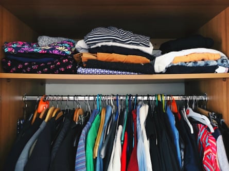 Closet containing colourful T-shirts and shirts on hangers and an upper shelf with orderly piles of folded clothes