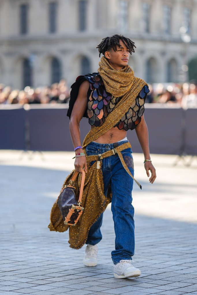 PARIS, FRANCE - OCTOBER 04: Jaden Smith wears a gold and black tweed with embroidered sequined scarf from Louis Vuitton, a gold and black tweed with embroidered sequined crossbody / belted long scarf, a black and burgundy embroidered yoke sleeveless / cropped top from Louis Vuitton, a brown LV monogram print pattern in coated canvas handbag from Louis Vuitton, navy blue denim large pants, a gold Love bracelet from Louis Vuitton, colored bracelets, white leather and pale gray sneakers from New Balance , outside Louis Vuitton, during Paris Fashion Week - Womenswear Spring/Summer 2023, on October 04, 2022 in Paris, France. (Photo by Edward Berthelot/Getty Images)