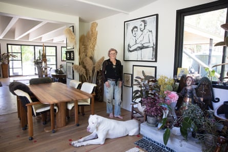 A woman stands in her dining room, next to a black-and-white artwork, with a large white dog lying at her feet