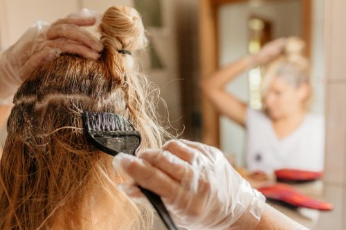 Rear view of woman dyeing hair in front of mirror at home