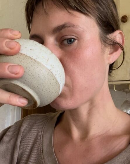 A woman drinking from a earthy-coloured clay bowl
