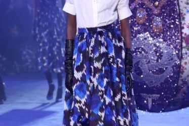 Model on the catwalk wearing white collared shirt, blue printed New Look-style skirt, black opera gloves.