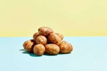 A pile of potatoes on a blue table top, yellow wall behind