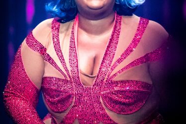 Lizzo appears onstage in a sparkly red catsuit. She wears her hair in a short flipped out bob with blue streaks.