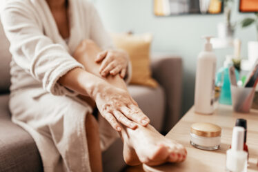 Close up of a woman applying lotion to her leg that's propped on a table.