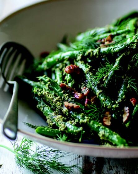 Close-up of a dish of green beans with a dill and pecan dressing.