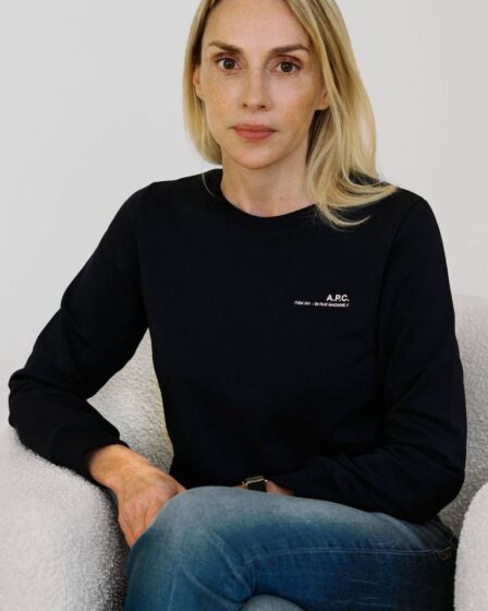 Invisible Collection co-founder Isabelle Dubern-Mallevays sits in an armchair, wearing a black jumper and blue denim jeans.