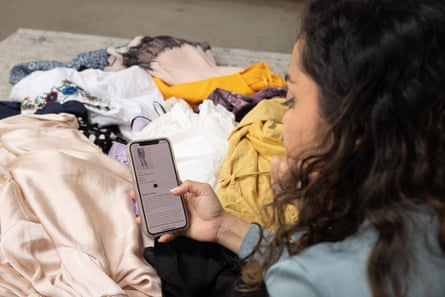 Karishma Luthria on her phone in front of a pile of clothes she no longer likes wearing