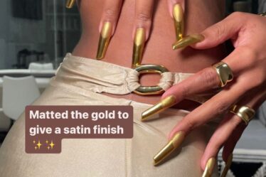 Megan Thee Stallion dressed in shiny gold holds her gold french manicure against her hip