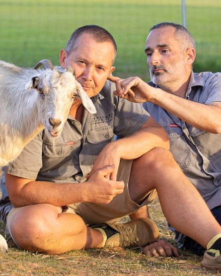 Jeff touches Todd’s ear as a goat stands beside them