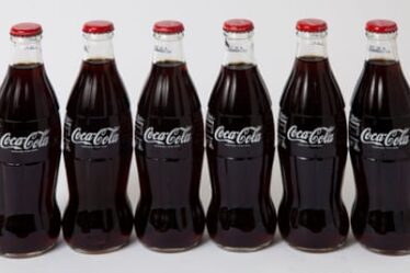 A row of six glass Coca-Cola bottles with red lids