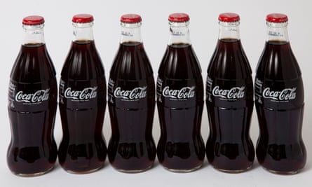 A row of six glass Coca-Cola bottles with red lids