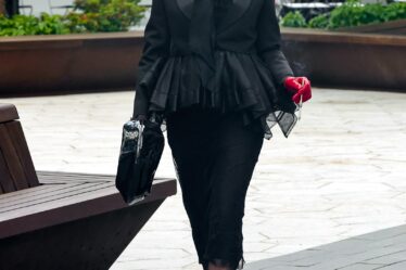 Cara Delevingne walks in New York wearing a black outfit red accessories and a dark brown wig with bangs