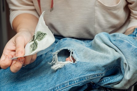 A woman mends jeans, sews a patch on a hole, hands close up.