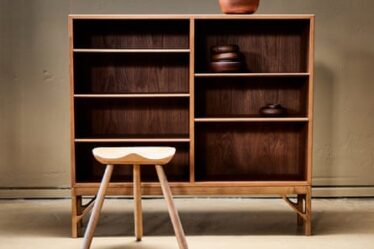 Børge Mogensen bookcase with teak bowlson it and a wooden three-legged stool in front