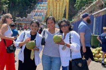 Two adult daughters and their mother pose with coconut drinks at Batu Caves in Gombak, Malaysia.