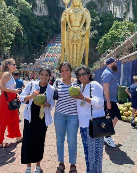 Two adult daughters and their mother pose with coconut drinks at Batu Caves in Gombak, Malaysia.