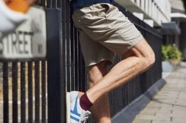 Man leaning against a iron fence, showing off the best ankle socks from London Sock Co. Blurry ankle in the top left.