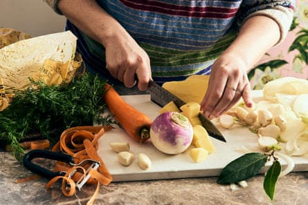 A person’s hands chopping up a swede on a chopping board, which is strewn with carrots and dill.