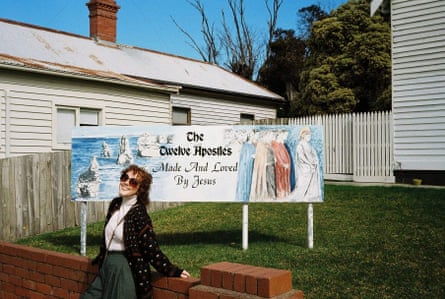 Tilly stands in front of a sign that reads 'The Twelve Apostles: Made And Loved By Jesus'