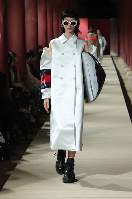 A Gucci model in a long white satin coat and black ankle boots