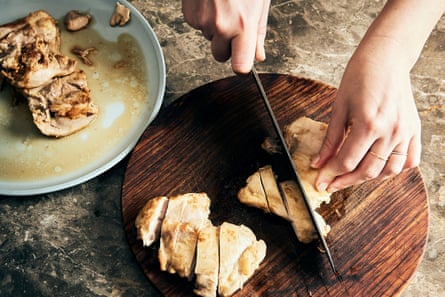 A hand slicing pan-fried chicken thighs on a round cutting board.