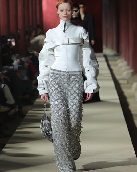 A model in a white high-neck blouse and grey bejewelled trousers