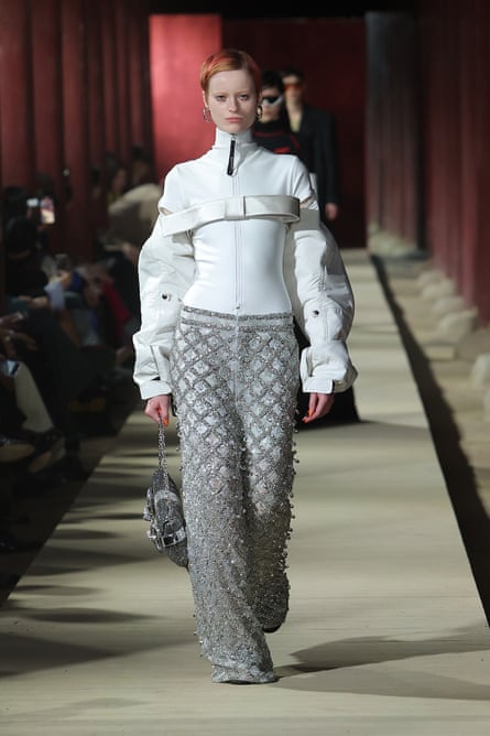 A model in a white high-neck blouse and grey bejewelled trousers