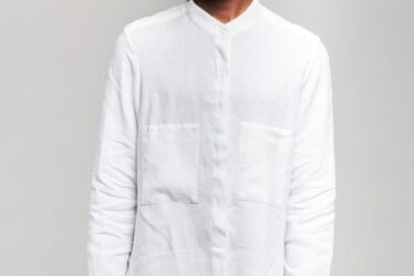 A male model in a white linen shirt standing against a grey background.