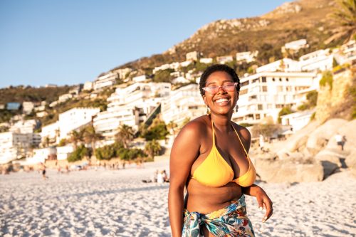 A happy woman on the beach wearing a yellow bikini and a colorful sarong